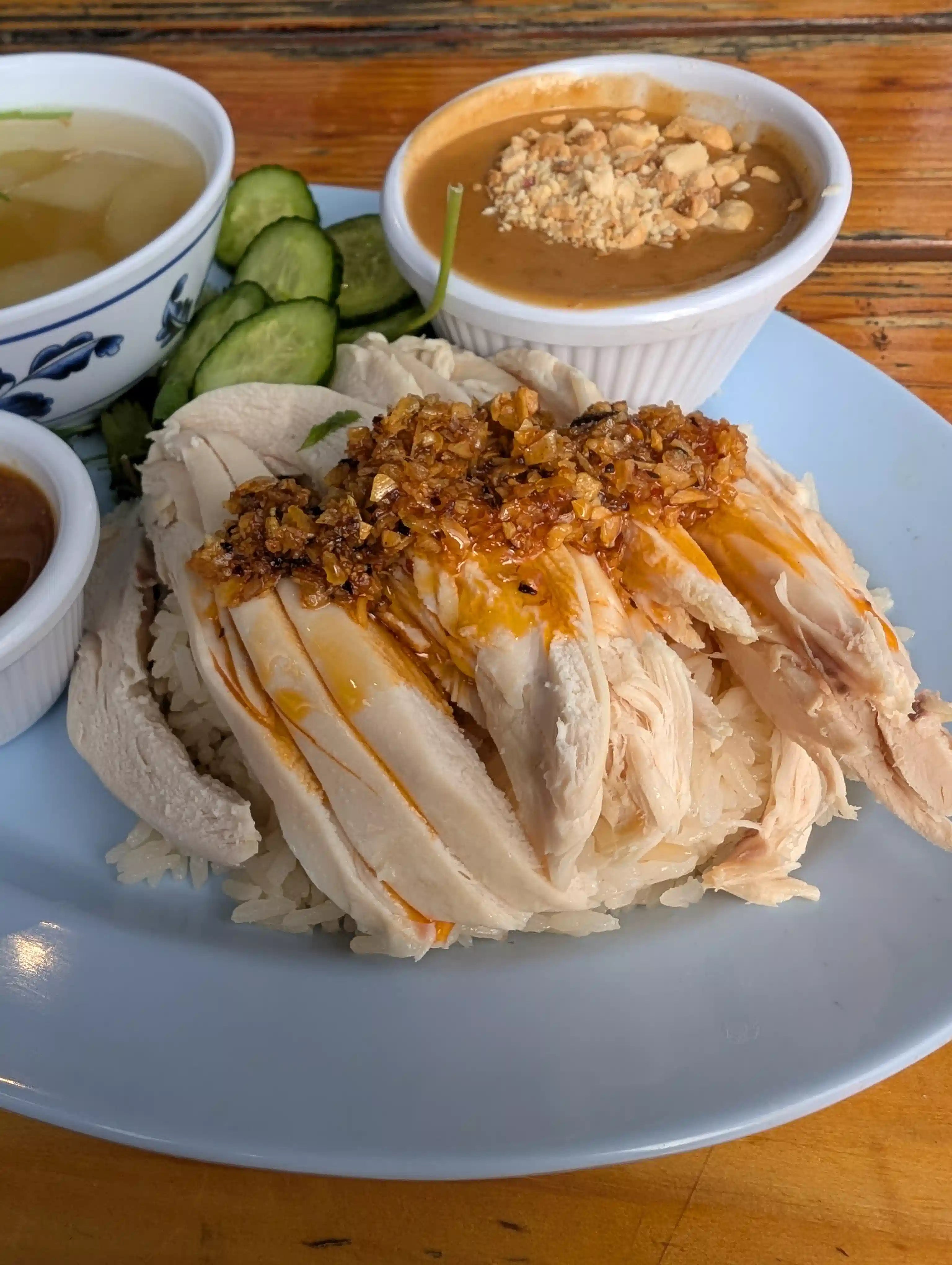 Plated dish of rice with chicken, chili oil, and a side of soup and pickles on a wooden table.